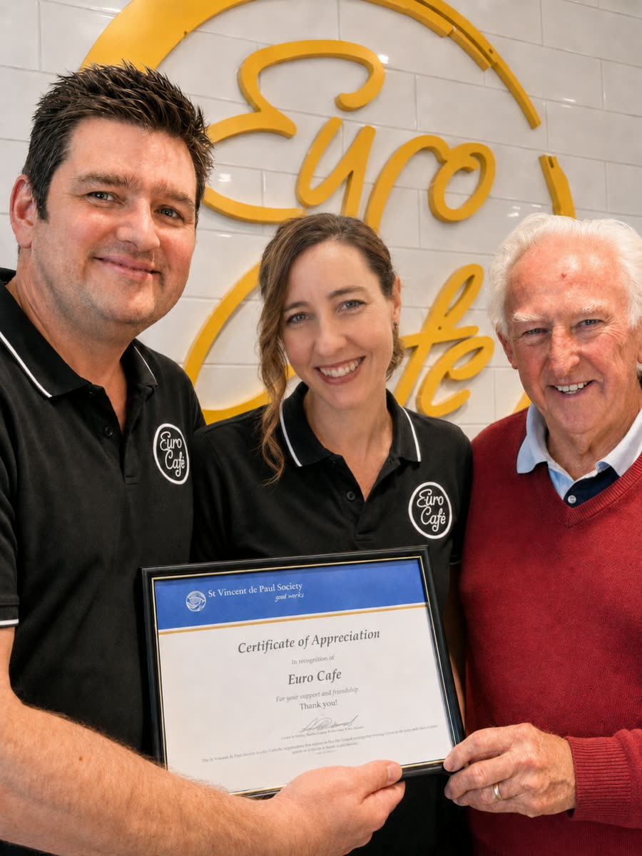 Richard and the Euro Cafe team in front of the gold Euro Cafe sign, holding a certificate of appreciation from the St Vincent de Paul Society